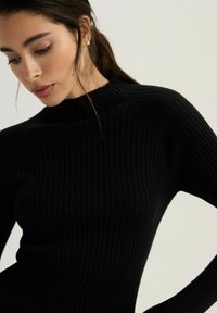 Czarny prążkowany sweter z golfem o dopasowanej sylwetce, wysokim dekolcie i długich rękawach. Miękka tekstura z pionowym wzorem.