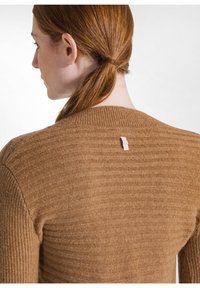 Brauner, gerippter Strickpullover mit Rundhalsausschnitt. Verfügt über ein kleines, hellrosa Etikett auf der Rückseite. Weiche Textur, körpernahe Passform.