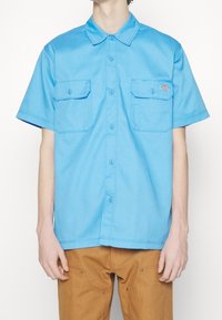 Lichtblauw overhemd met korte mouwen, een puntige kraag, twee borstzakken en knoopsluiting. Gemaakt van een gladde stof met een casual pasvorm.
