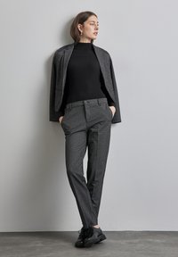 Maglione a collo alto nero a coste abbinato a un blazer texturizzato bianco e nero e pantaloni coordinati, completato con calzature nere.