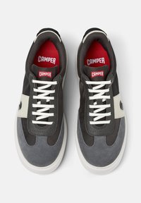 Dark gray and black sneakers with white laces, featuring a red logo on the tongue and a gray suede panel on the side.