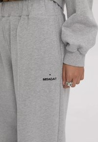 Grijze sweatpants met een elastische tailleband, zijzakken en het zwarte "MISAGA®" logo nabij de zoom. Zachte textuur en een losse pasvorm.