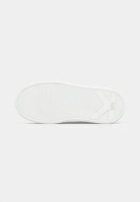 Sola do sneaker branca com padrão texturado antideslizante e logótipo em relevo "KARL LAGERFELD" perto do calcanhar em fundo simples.