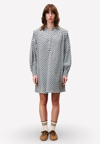 Hemdblusenkleid mit einem blau-weißen Karomuster, Ballonärmeln und einer Länge bis zur Mitte des Oberschenkels. Getragen mit beigen Schuhen und gestreiften Socken.