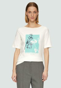 T-shirt en coton blanc à manches courtes, avec un design graphique turquoise comportant des éléments floraux et le texte « ELEVATED EVERYDAY » en bleu.