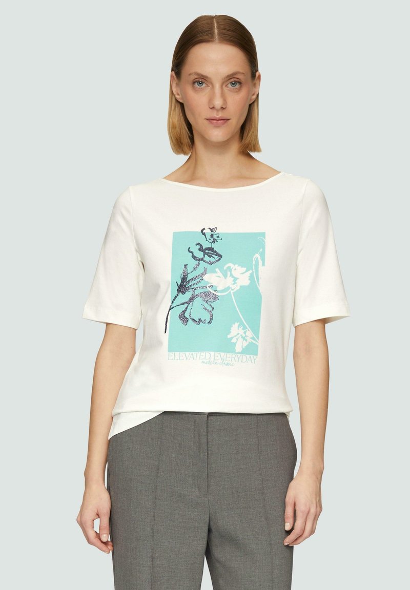 T-shirt en coton blanc à manches courtes, avec un design graphique turquoise comportant des éléments floraux et le texte « ELEVATED EVERYDAY » en bleu.