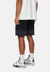 Pantaloni corti neri sfumati con tasche laterali, tessuto morbido e vestibilità comoda, abbinati a sneakers bianche e grigie con accenti neri.