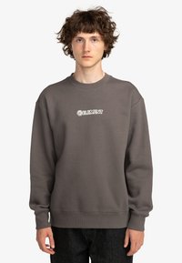 Sudadera gris con cuello redondo y mangas largas. Presenta un logo blanco de "ELEMENT" en el pecho. Está hecha de una tela suave y texturizada.