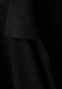 Gros plan d'un tissu tricoté noir avec un rabat plié montrant les détails de la texture et du tissage sur un fond sombre.