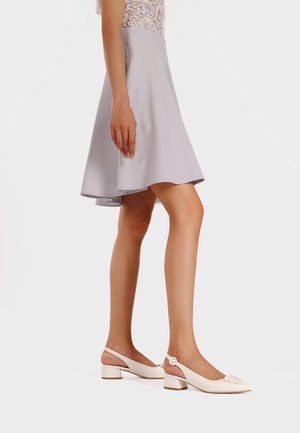 Una gonna svasata di un grigio chiaro abbinata a scarpe slingback color crema con tacco a blocco e un accento decorativo sulla punta.