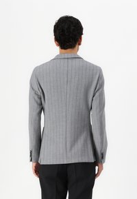 Blazer grigio a righe con vestibilità slim, spalle strutturate, rever a notched e chiusura con un bottone. Presenta due spacchi posteriori e polsini con bottone.
