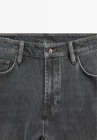 Jeans in denim grigio scuro con chiusura a bottone, design a cinque tasche e cuciture a contrasto. Il materiale è robusto e ha una texture liscia.