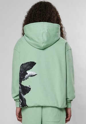Mintgrön oversized hoodie med en känguruficka, med ett svartvitt grafiskt mönster på vänster sida. Mjuk bomullsmaterial.