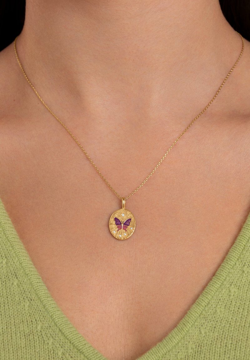Gouden hangerketting met een cirkelvormig ontwerp, voorzien van een paarse vlinder en kleine decoratieve steentjes, hangend aan een dunne gouden ketting.