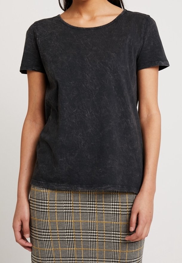 Femme portant un t-shirt noir délavé à manches courtes et une jupe à carreaux taille haute avec des motifs beige, noir et blanc.