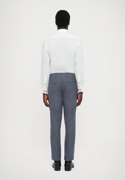 White long-sleeve shirt with buttoned cuffs, paired with gray textured pants and black shoes, viewed from the back.