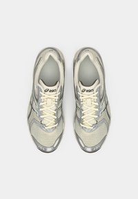 Lys grå ASICS løpesko med mesh-overdel, kremfargede detaljer og teksturert såle. Har lisser og reflekterende detaljer.