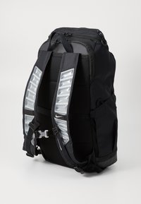 Sac à dos noir avec des bretelles rembourrées et un détail transparent, compartiment principal zippé, et plusieurs poches externes pour le rangement.