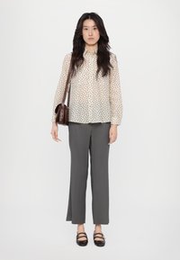 Long-sleeve, sheer blouse with a leaf print, paired with high-waisted, straight-leg gray trousers. Brown shoulder bag and black flats with straps.