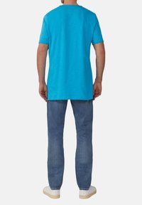 T�ürkises T-Shirt mit kurzen Ärmeln und Rundhalsausschnitt, kombiniert mit hellblauen Jeans und weißen Turnschuhen. Einfaches, lässiges Design.