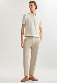 Lichtbeige gebreide poloshirt met korte mouwen, gecombineerd met beige broeken en bruin instap-schoenen, met gestructureerde stofdetails.