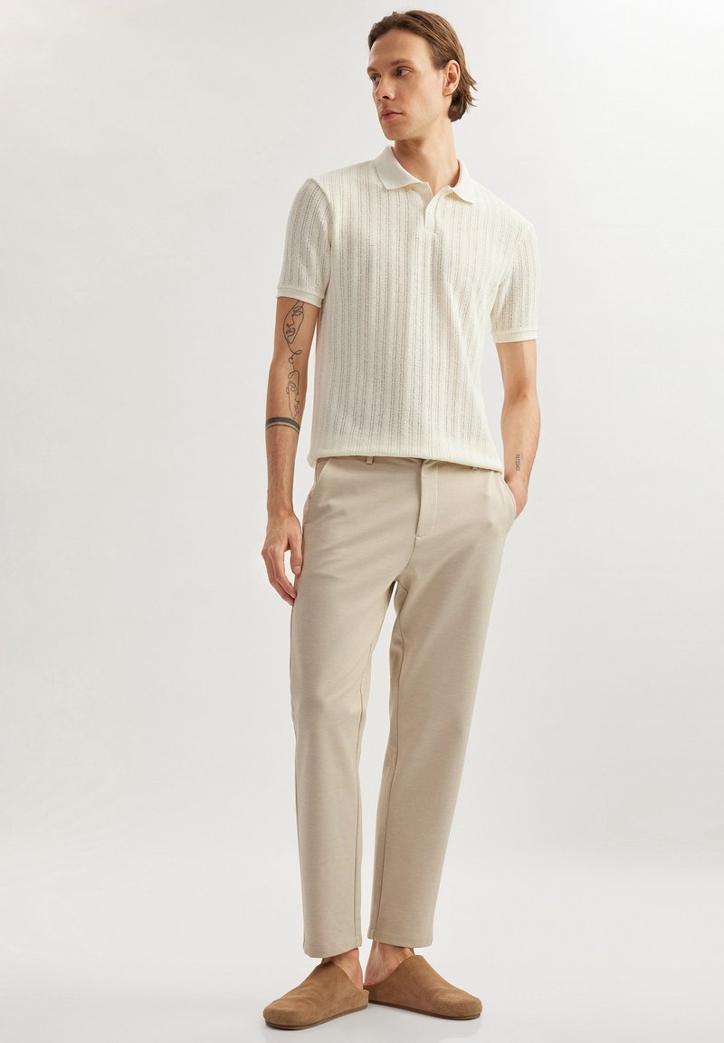 Lichtbeige gebreide poloshirt met korte mouwen, gecombineerd met beige broeken en bruin instap-schoenen, met gestructureerde stofdetails.