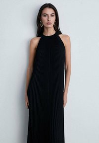 Mustat pleated-halter-mekko, jossa on pystysuorat poimut, istuva yläosa ja virtaava siluetti, suunniteltu minimalistiseen estetiikkaan.