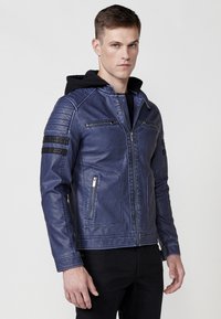 Chaqueta de cuero azul con cierre frontal, dos bolsillos en el pecho, franjas negras horizontales en las mangas y una capucha debajo del cuello.