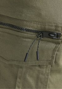 Svart dragkedja med dubbla svarta dragsnören på olivgrön tygficka med synlig flat sömnad.