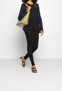 Námorníková cardigan přes černý top na ramínka, v kombinaci s černými skinny džíny a černými sandály na podpatku. Drží olivově zelenou kabelku přes rameno.