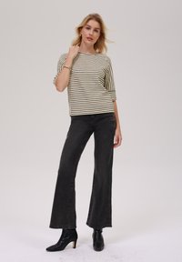 Striped, short-sleeve top in cream and black, paired with high-waisted, flared black jeans and black heeled boots. Smooth fabric with a relaxed fit.