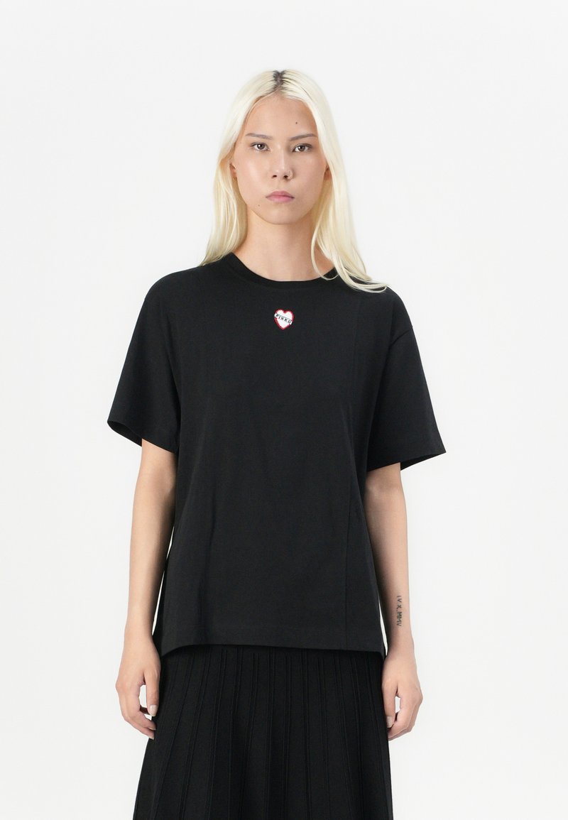 T-shirt nera in cotone con maniche corte, che presenta un piccolo logo a forma di cuore rosso e bianco sul petto. Taglio dritto e design casual.