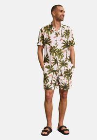 Camicetta bianca a maniche corte con colletto e pantaloni corti abbinati, con motivi di palme verdi e fiori rossi; vestibilità comoda, tessuto leggero.
