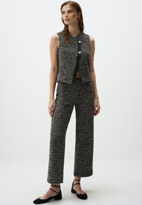 Graue Tweed-Ärmellose Weste mit einem vorderen Schlitz und zwei Knöpfen, kombiniert mit weiten Hosen aus demselben Stoff und schwarzen Ballerinas.