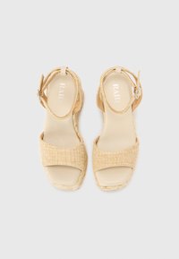 Sandalias de cuña beige con detalles de paja trenzada, punta abierta, tira en el tobillo con hebilla y forro interior suave. Logo de la marca visible en el interior.