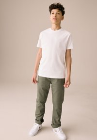 Biała bawełniana koszulka zestawiona z oliwkowozielonymi spodniami i białymi trampkami. Strój charakteryzuje się prostym, casualowym designem i luźnym krojem.