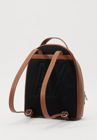 Tiras y acentos de cuero marrón en una mochila negra de malla texturizada que presenta un logo prominente, con una forma redondeada y cierre de cremallera.
