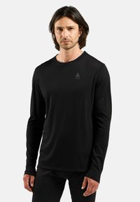 Black long-sleeve shirt made of soft fabric with a rounded neck. Features a subtle logo on the chest and fitted sleeves.