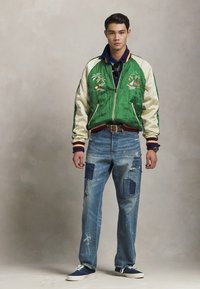 Grön bomberjacka med satinärmar, broderade palmträd, matchad med slitna blå jeans med lappar och en avslappnad passform.