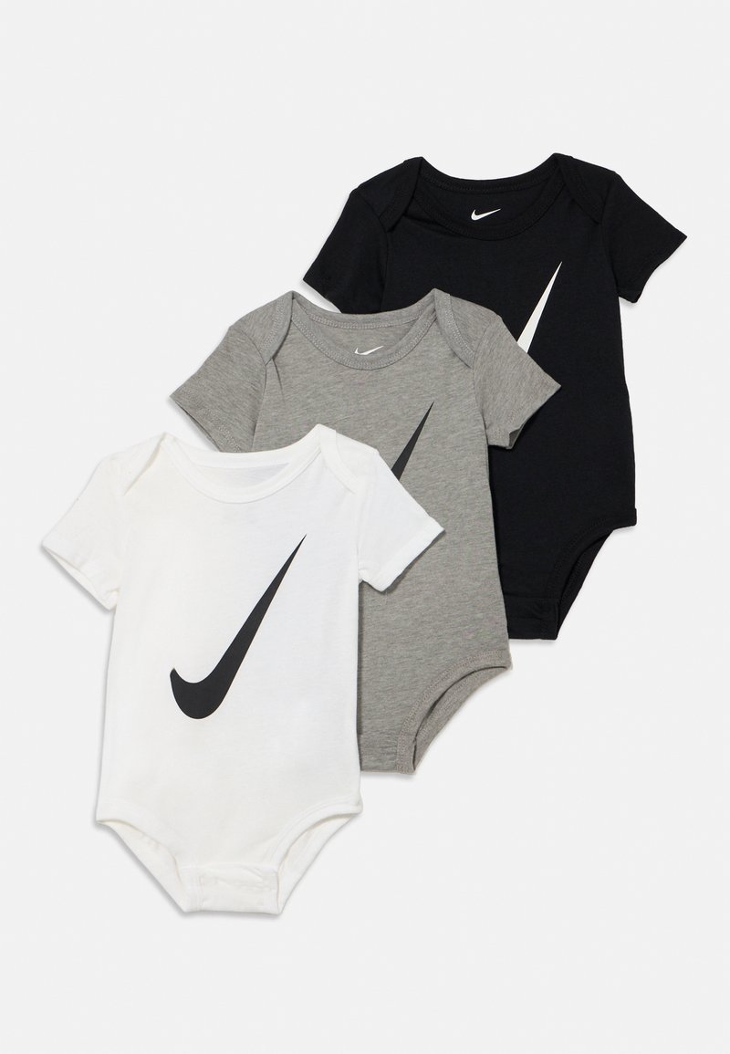 Três bodies de bebé em algodão branco, cinzento e preto. Cada um apresenta um destacado logótipo da Nike swoosh preto na parte da frente.