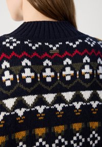 Tumesinine kootud svetter, millel on Fair Isle muster valgete, punaste, roheliste ja kollaste aktsentidega. Ribitud krae ja väike logo silt taga.