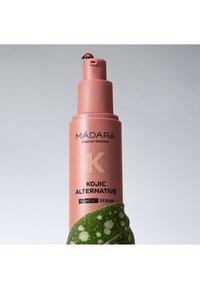 Bottiglia di siero cilindrica di colore rosa chiaro con testo e etichetta scuri; presenta una foglia verde avvolta attorno alla base e una coccinella sulla cima.