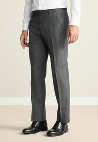 Gray houndstooth patterned trousers made of textured fabric, featuring a slim fit and single pleat design, paired with black dress shoes.