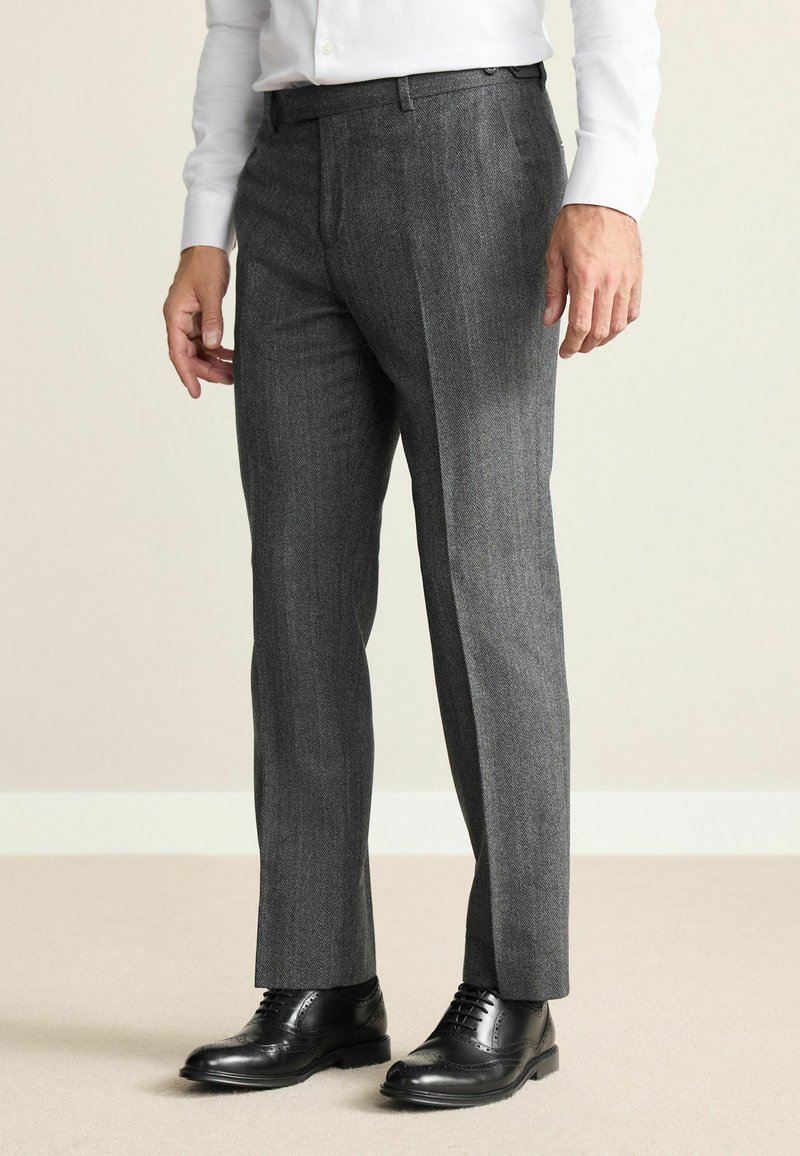Gray houndstooth patterned trousers made of textured fabric, featuring a slim fit and single pleat design, paired with black dress shoes.