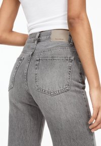 Jeans din denim gri cu talie înaltă, având un patch din piele inscripționat "PULL&BEAR" și două buzunare la spate. Țesătura are un finisaj texturat.