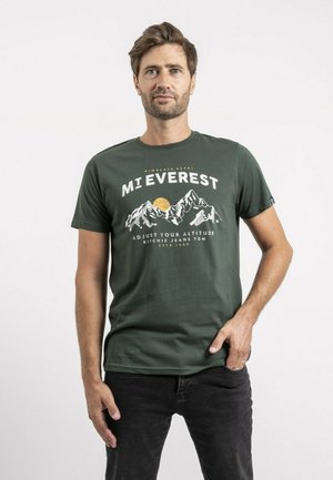 T-shirt en coton vert foncé avec un design graphique représentant des montagnes, un soleil et le texte "MI EVEREST" en blanc et jaune. Manches courtes, col rond.
