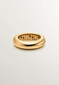 Anillo de oro con un exterior liso y redondeado y una banda interior perforada con patrones circulares. El acabado pulido realza el brillo.