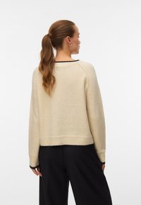 Crèmekleurige gebreide trui met een ronde hals, verlaagde schouders en geribbelde zoom. Heeft zwarte accenten bij de halslijn en manchetten.