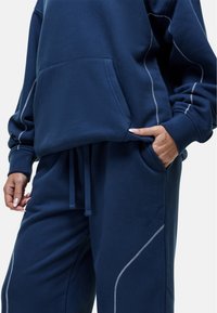 Navyblauwe sweatshirt en sweatpants set in zachte stof, met een voorkantzak, een tailleband met trekkoord en witte stiksels.
