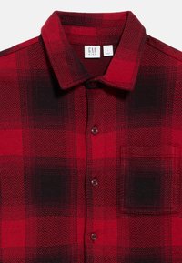 Červená a čierna károvaná košeľa na zapínanie s golierom, obsahujúca vrecko a textúrovanú látku v kockovanom vzore.